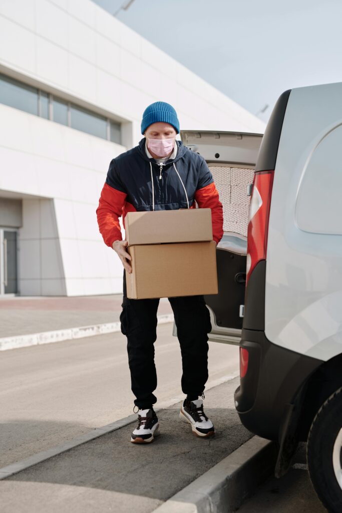 A delivery worker wearing a face mask unloading packages from a van in an urban area.